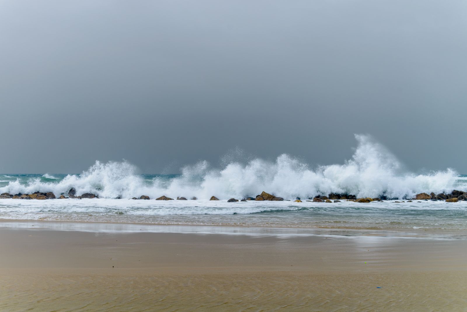 Heavy surf breaking on a sandy beach under a gray, stormy sky