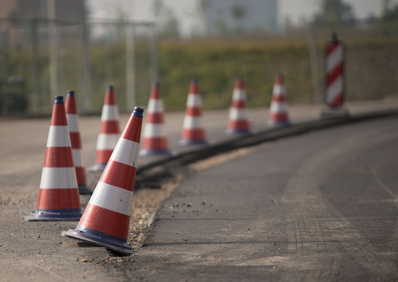 Row of orange and white traffic cones along the edge of a freshly paved road under construction